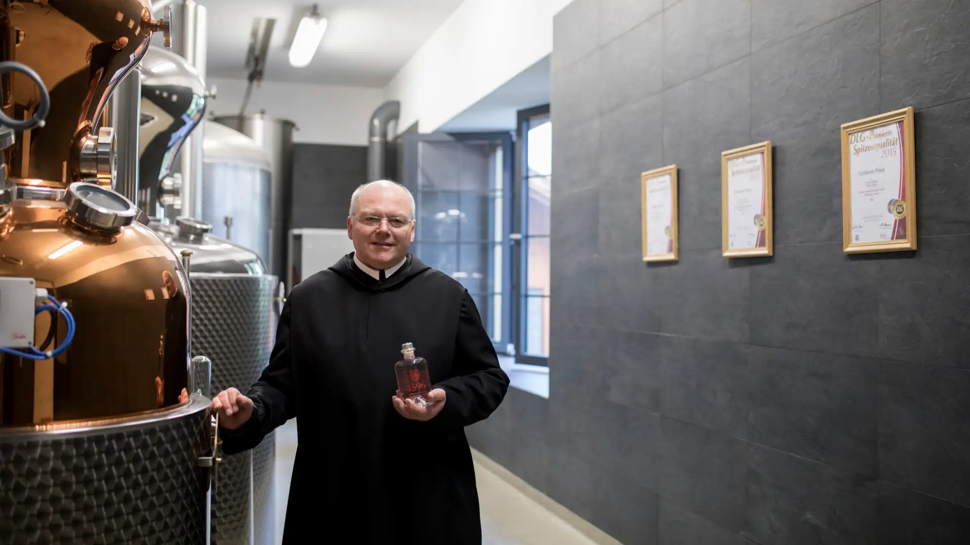 Abt vor Destillerietank mit Gin in der Hand